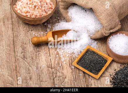 Mix di diversi tipi di sale su sfondo di legno. Sali marini, cristalli di sale himalayano nero e rosa, collezione di diversi tipi di salt.in la borsa Foto Stock