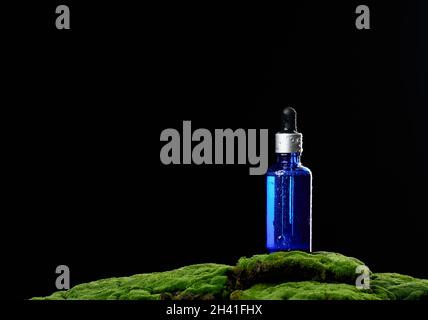 Flacone in vetro con portapipette su muschio verde, sfondo nero Foto Stock