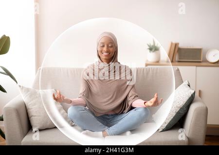 Felice felice millennial african american signora in hijab medita in soggiorno interno in bolla di protezione Foto Stock