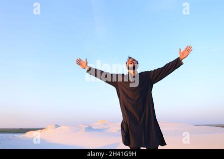 Felice ritratto di maschio arabo, che sorride e si rallegra nella vita, in piedi in mezzo al largo deserto in una sera limpida. Foto Stock