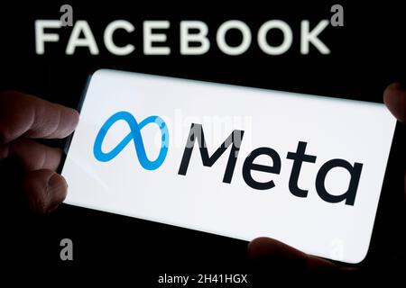 LOGO DELLA META azienda DI FACEBOOK visto smartphone tenere in mano con logo sfocato di Facebook inc. Sullo schermo del laptop dietro. Messa a fuoco selettiva. Stafford, Ki Foto Stock