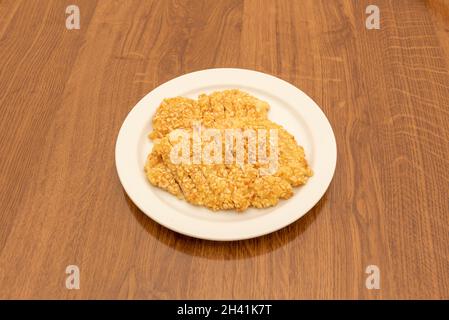 Filetti di pollo in pastella con mandorle tritate su piatto bianco e tavola di legno Foto Stock