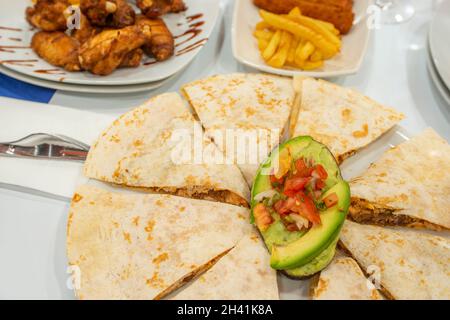 Quesadillas messicane farcite con stufato di tinga di pollo con avocado maturo, un cucchiaio da tavola di Pico de gallo e altri piatti sullo sfondo Foto Stock