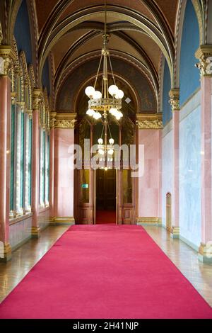 BUDAPEST, UNGHERIA - 03 MAR 2019: Lungo corridoio con tappeto rosso su pavimento in marmo e lampadario sul soffitto nell'edificio del Parlamento ungherese Foto Stock