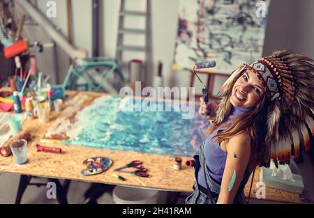 Una giovane artista femminile con un cofano da guerra in un'atmosfera piacevole nello studio sta posando per una foto mentre lavora ad un nuovo dipinto. Arte, pittura, s Foto Stock