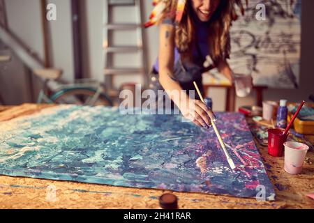 Una giovane artista femminile con un cofano di guerra in un'atmosfera creativa nello studio sta lavorando ad una pittura astratta. Arte, pittura, studio Foto Stock