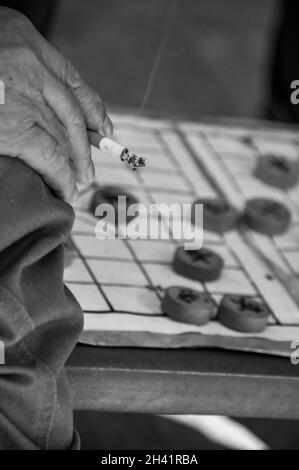 Una mano di un vecchio uomo che tiene una sigaretta mentre gioca a scacchi cinesi nello Zhongshan Park di Shanghai, in Cina. Foto Stock