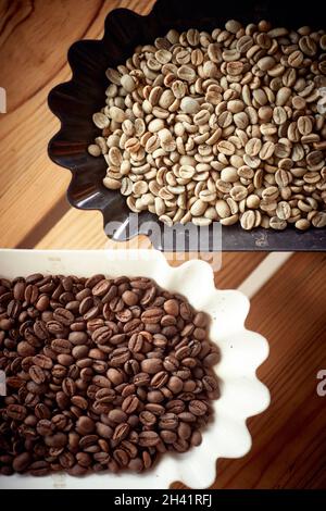 Vista dall'alto di chicchi di caffè crudi e torrefatti fragranti e aromatici in contenitori ben disposti sul tavolo. Caffè, bevande, produzione Foto Stock