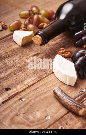 Bottiglia di vino con cavatappi. Con uva, fetta di camembert di formaggio, noce su fondo vecchio tavolo grigio in calcestruzzo con spazio copia. Vino rosso con un'acquavite di vite Foto Stock