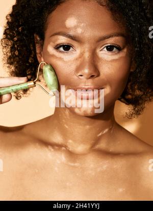 rullo di giada facciale. Una donna massaggia il viso con un rullo di giada verde per una pelle elastica perfetta Foto Stock