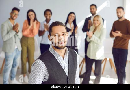 Ritratto di giovane uomo riuscito e intelligente su sfondo sfocato di persone che lo applaudono. Foto Stock