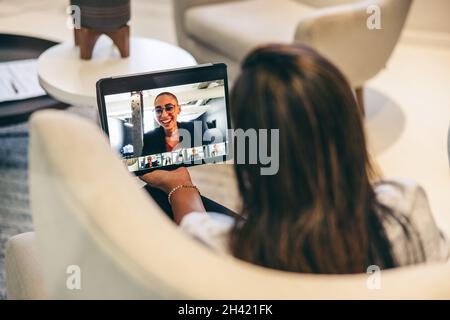 Retroguview di una donna d'affari che partecipa ad una videoconferenza in un ufficio. Donna d'affari anonima che usa un tablet digitale per un incontro virtuale con la sua p Foto Stock