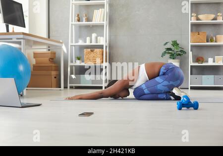 Donna afroamericana che fa esercizi sportivi a casa di fronte al portatile durante la trasmissione online. Foto Stock