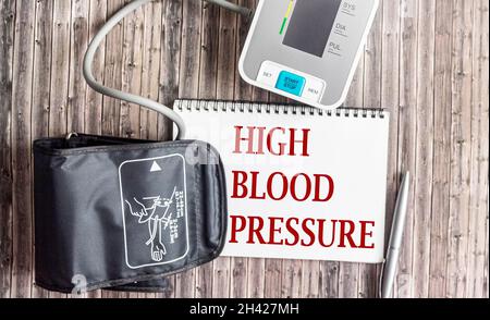 Tonometro medico per la misurazione della pressione sanguigna, su sfondo di legno. Il testo alta pressione sanguigna è scritto su un pezzo di carta bianco Foto Stock