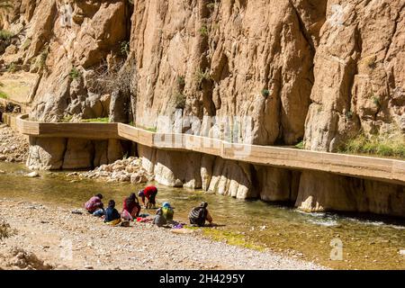 Todra, Marocco - 25 febbraio 2019: Donne con bambini (non identificabili) in costumi colorati stanno facendo lavanderia sul lato del fiume nel famoso Todra Foto Stock