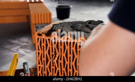 Lavoratore mette cemento su un mattone su un cantiere. Riprese in stock. Muratore che posa mattoni per fare un muro, sta mettendo la Malta sulla cima di un mattone. Foto Stock