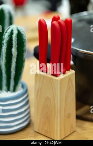 Set coltelli rossi da cucina in acciaio inox per affettare la carne in un contenitore in legno, posto su un tavolo in cucina. Blocco coltelli nel contatore legno Foto Stock