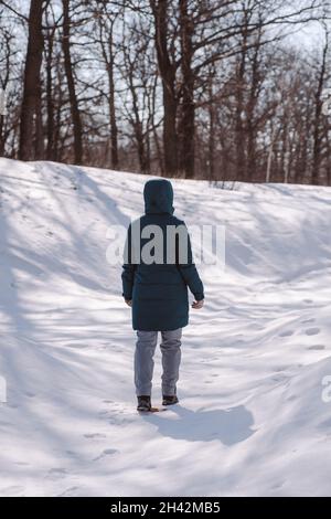 La giovane donna cammina nella foresta. Donna caucasica stand su strada tra gli alberi in foresta innevata e godere del sole, vista posteriore Foto Stock