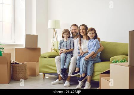 Ritratto di famiglia felice seduta sul divano tra scatole di cartone in salotto della loro nuova casa. Foto Stock