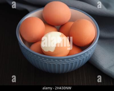 Un uovo sodo incrinato con altre uova sode intorno ad esso in una ciotola. Primo piano. Foto Stock