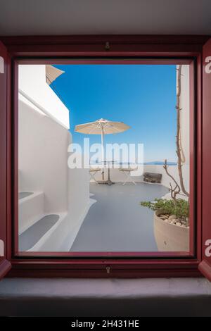 Vista sulla terrazza con ombrellone, scrivania e sedie dalla finestra Foto Stock