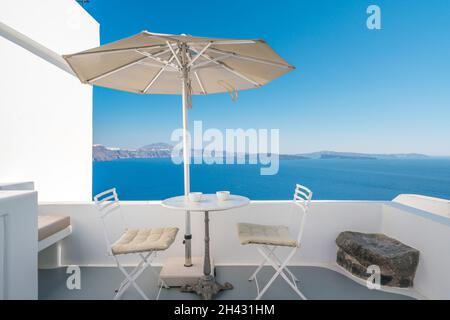 Terrazza all'aperto con ombrellone, scrivania e sedie contro i blu marino sull'isola di Santorini, Grecia Foto Stock