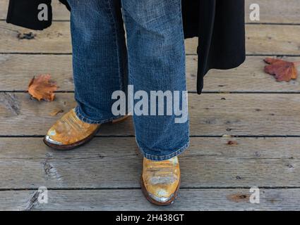 Stivali da cowboy e jeans, dettagli ravvicinati dell'abbigliamento in stile occidentale per uomo all'aperto. Stagione autunnale. Vista stradale, messa a fuoco selettiva. Foto Stock