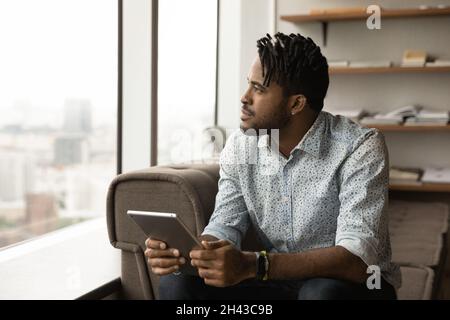 Giovane africano pensieroso e sognante che tiene un tablet digitale. Foto Stock