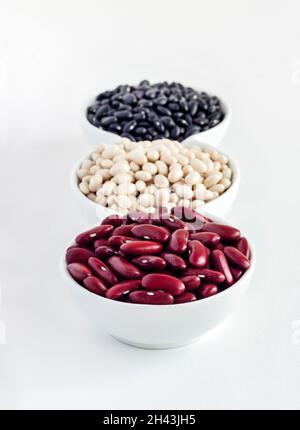 Assortimento di fagioli in un recipiente bianco su sfondo bianco. Fagioli rossi, fagioli bianchi e fagioli neri Foto Stock