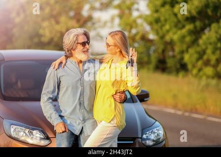 Felice coppia matura con chiavi vicino auto in campagna Foto Stock