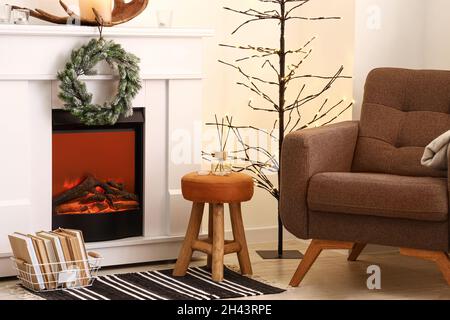 Caminetto elettrico e comoda poltrona in camera decorata per Natale Foto Stock