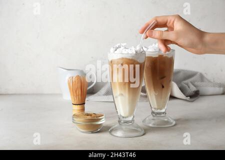 Mano femmina con bicchieri di hojicha latte ghiacciato su sfondo chiaro Foto Stock