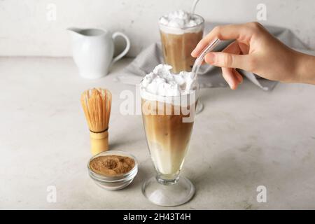 Mano femmina con bicchieri di hojicha latte ghiacciato su sfondo chiaro Foto Stock