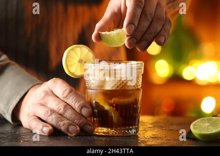 Barman maschio che spreme calce in un bicchiere di gustoso cocktail Cuba Libre al tavolo del bar Foto Stock