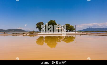 Vista aerea della vecchia chiesa ortodossa e degli alberi nel mezzo di saline di colore giallo nella Grecia occidentale Foto Stock