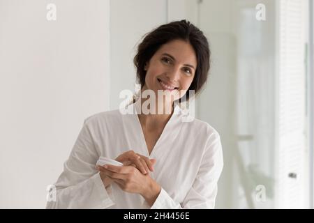 Latina donna in accappatoio contiene vasetto applicazione crema mani Foto Stock