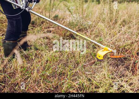 Giardiniere che taglia le erbacce con il decespugliatore. Operatore che taglia erba secca con un tagliabasette manuale a benzina con disco a lame in metallo Foto Stock