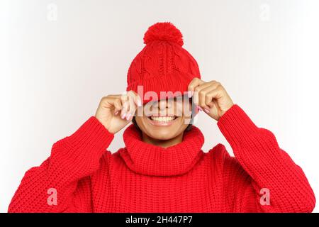 Divertente ragazza nera nascondere gli occhi sotto cappello di maglia di tendenza felice sorridente. La donna africana gioiosa ha divertimento Foto Stock