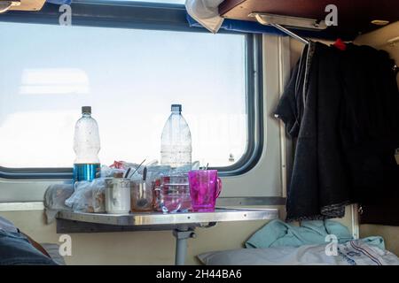 Bottiglie d'acqua di plastica, tazze e bicchieri su un tavolo in terza classe in auto condivisa, platzcart carrozza nel treno operato da Kazakhstan Temir Zholy Foto Stock