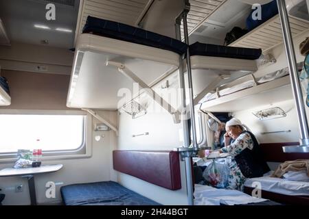 Anziana donna kazako seduta in 3 classe auto, carrozza platzcart nel treno operato da Kazakhstan Temir Zholy Foto Stock