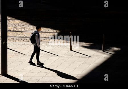 Belgrado, Serbia - 26 ottobre 2020: Un ragazzino in piedi da solo in attesa di un tram sulla fermata dell'autobus alla luce del sole, vista ad angolo alto da dietro, con statura Foto Stock