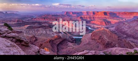 La luce soffusa dell'ora d'oro soffusa colpisce il fiume Colorado Gooseneck, con fumo nei canyon del fiume Colorado in lontananza al Dead Horse Point state Par Foto Stock