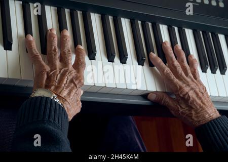 Primo piano le mani dell'uomo anziano sui tasti del pianoforte Foto Stock