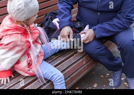 un uomo mette le ginocchiere sulle gambe della figlia prima di pattinare Foto Stock