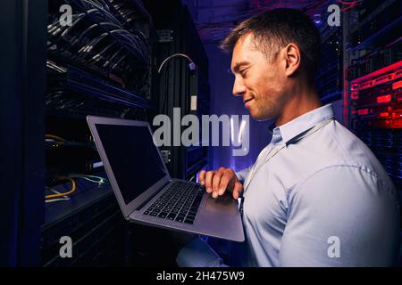 Sorridente soddisfatto amministratore di sistema che controlla le prestazioni del server Foto Stock