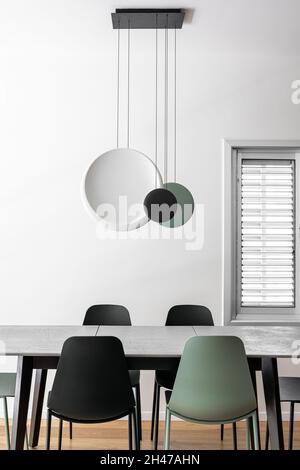 Sala da pranzo in appartamento con tavolo da pranzo e sedie e illuminazione appesa al soffitto, in verde oliva, bianco e nero Foto Stock
