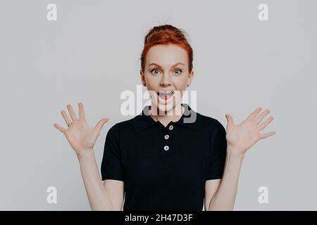 Giovane ragazza sorpreso emotivo zenzero alzando le mani e bocca di apertura con espressione del volto scioccato Foto Stock