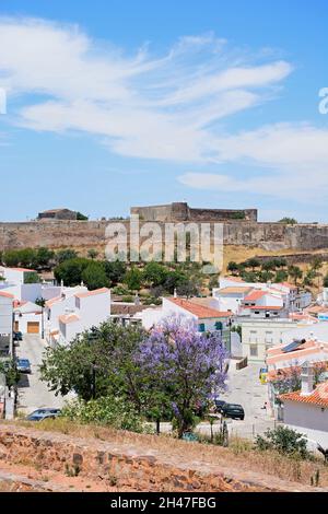 Vista in elevazione del castello e la città di edifici con una graziosa struttura Jacaranda in piena fioritura in primo piano, Castro Marim, Algarve, Portogallo, dell'Europa. Foto Stock