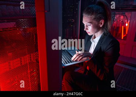 Tecnico femminile che utilizza il laptop per analizzare il server Foto Stock