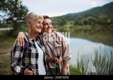 Happy anziano escursionista madre abbracciando con la figlia adulto quando si guarda il lago all'aperto in natura Foto Stock